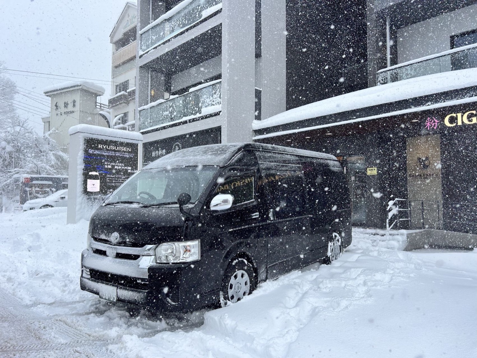 Private 9-seat minibus transfer outside a Hakuba hotel during heavy snowfall